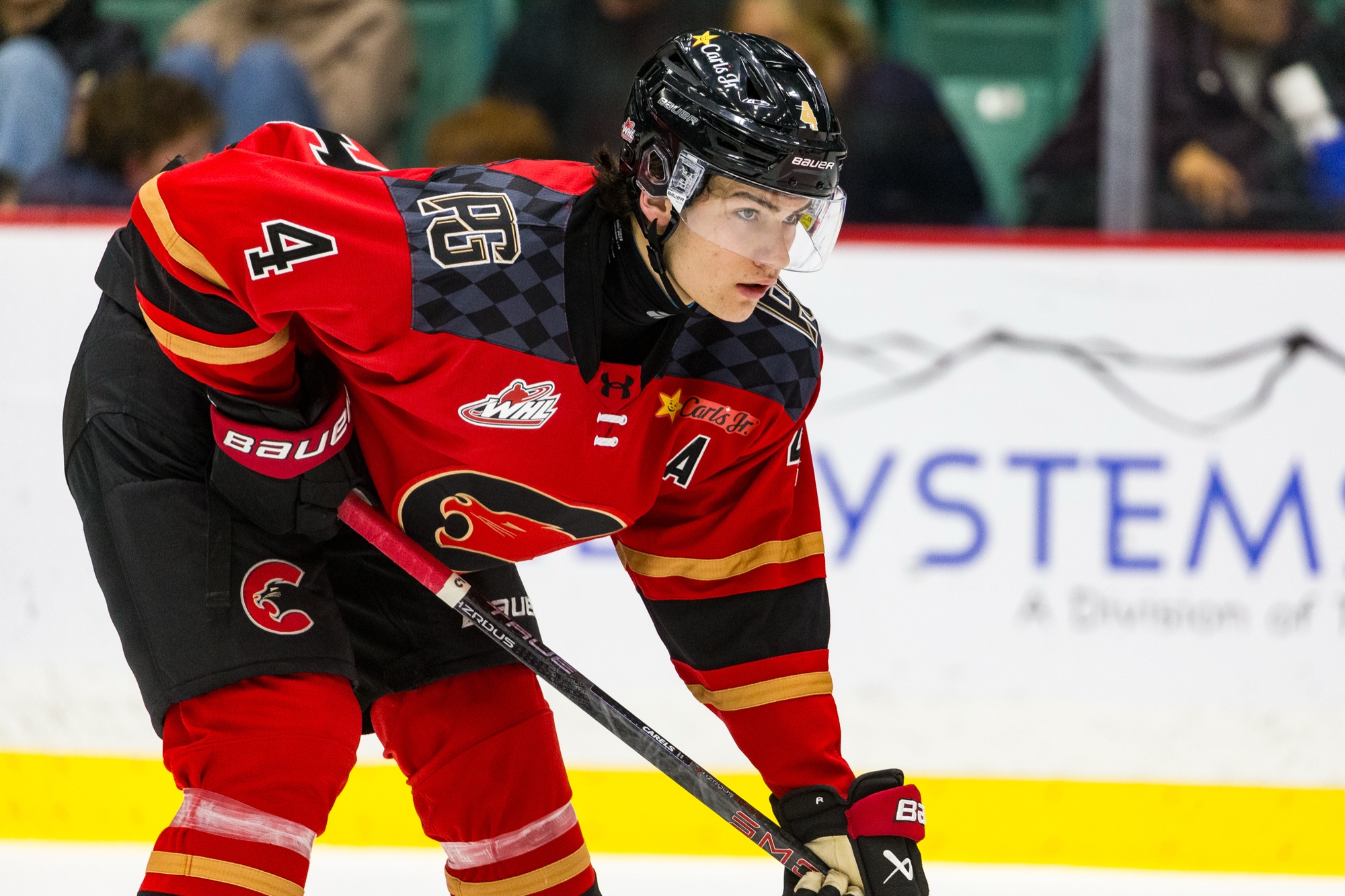 Carson Carels wearing No. 4 for the Prince George Cougars, crouched at a faceoff in the red home jersey with the assistant captain's A.