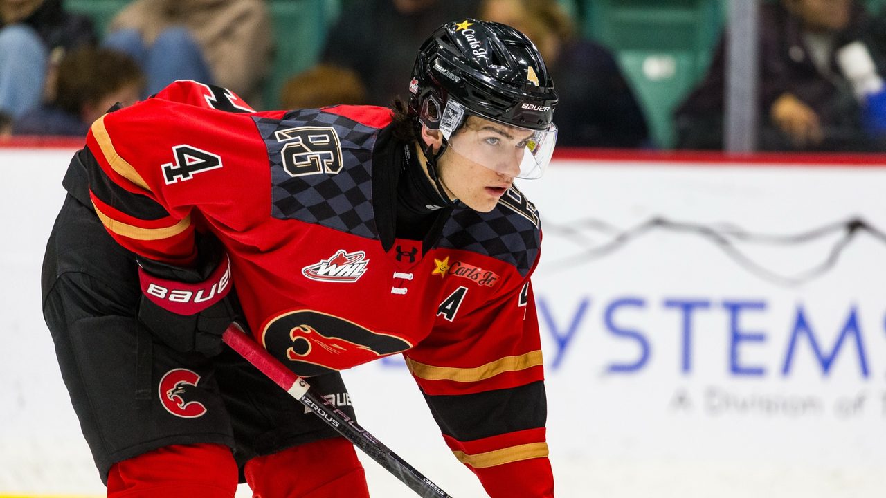 Carson Carels wearing No. 4 for the Prince George Cougars, crouched at a faceoff in the red home jersey with the assistant captain's A.