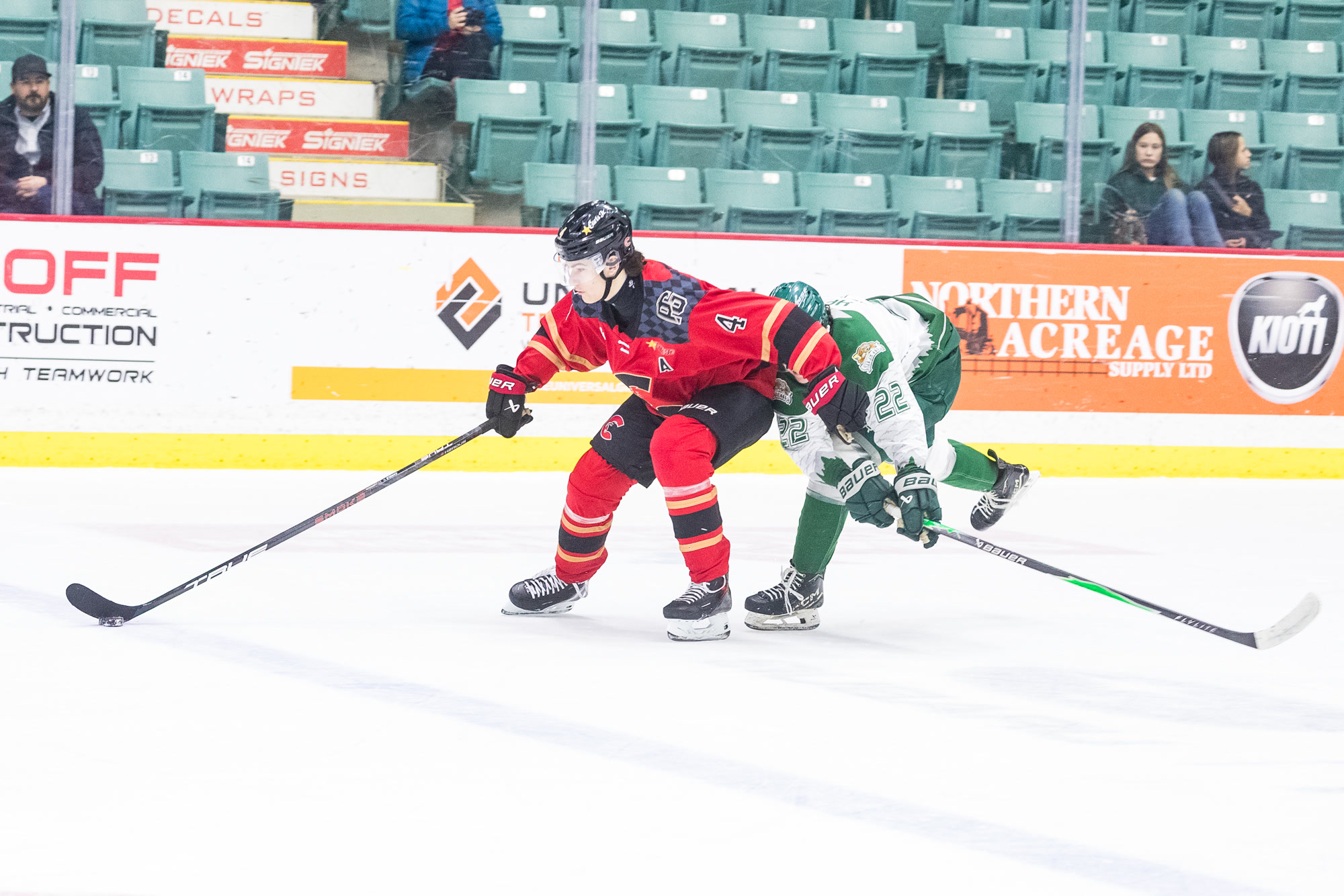 Carson Carels in the Prince George Cougars red home jersey, No. 4 with an assistant captain's A, driving the puck up ice with an opposing forward draped across his back.
