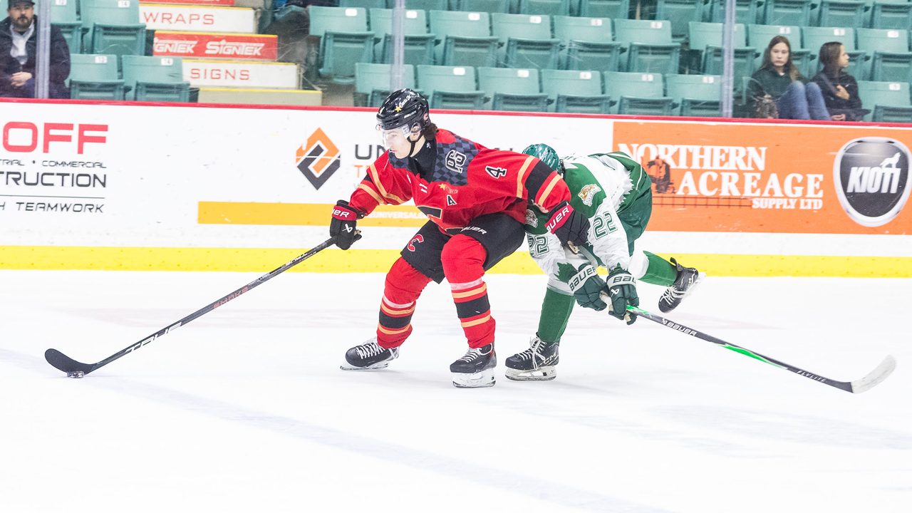 Carson Carels in the Prince George Cougars red home jersey, No. 4 with an assistant captain's A, driving the puck up ice with an opposing forward draped across his back.